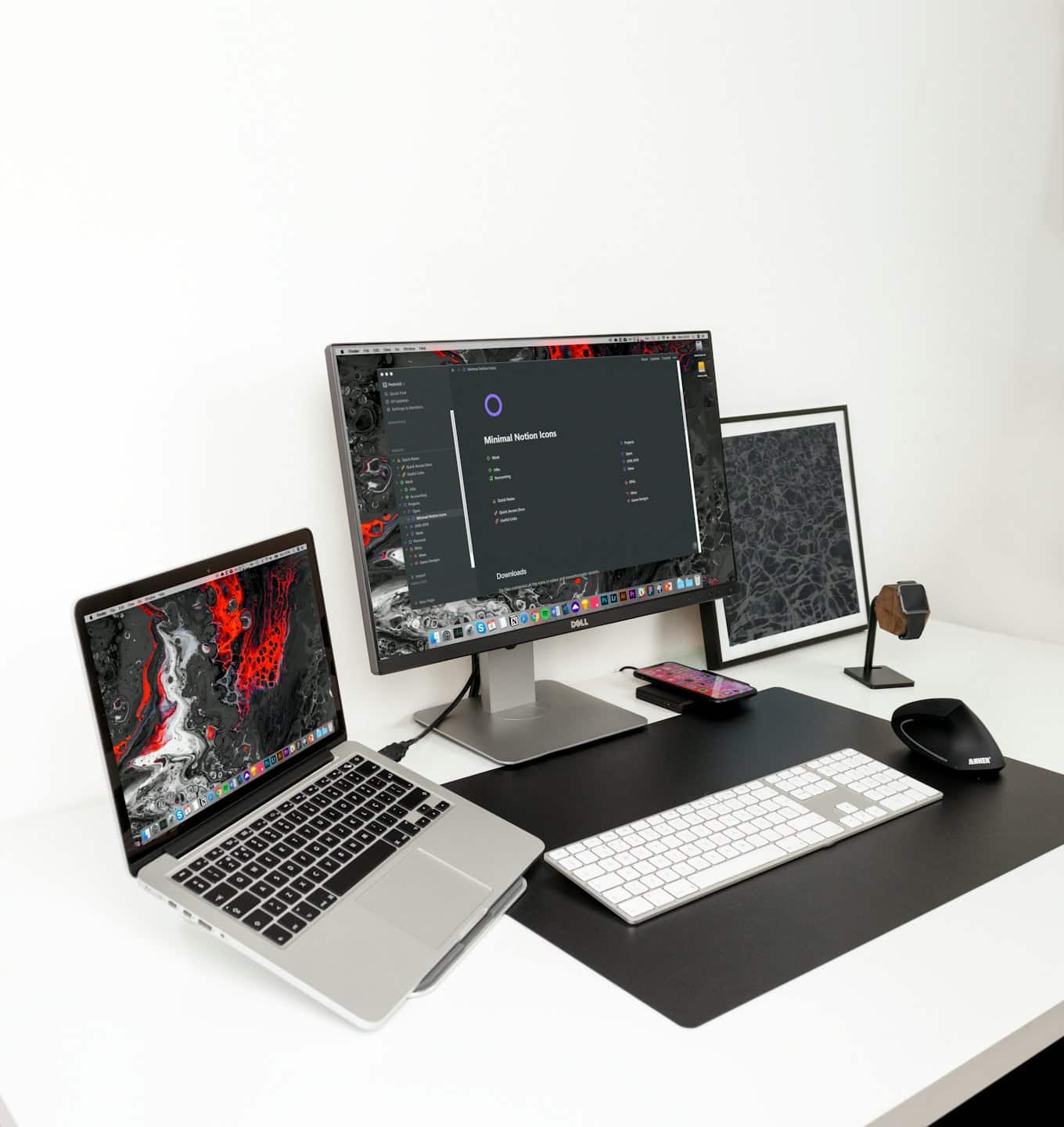 Spazio di lavoro minimalista con laptop, monitor e accessori da scrivania su una scrivania bianca.